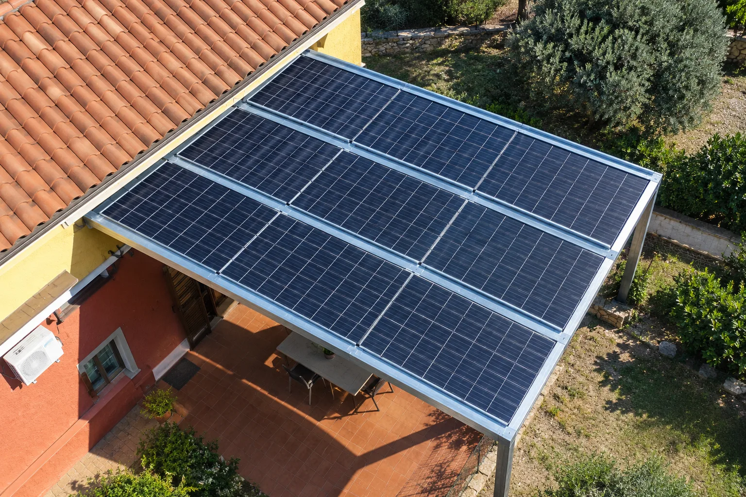 Vista dall'alto della pergola fotovoltaica addossata alla casa, con i moduli che coprono la terrazza pavimentata di fianco al tetto in coppi